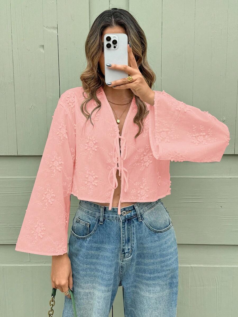 Person wearing a pink lace top and blue jeans against a green wall.