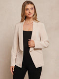 Woman wearing a beige blazer over a black top against a beige background