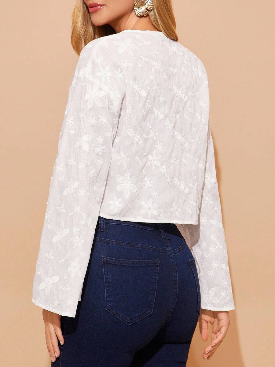 White blouse with long sleeves and a pattern, worn by a person against a beige background