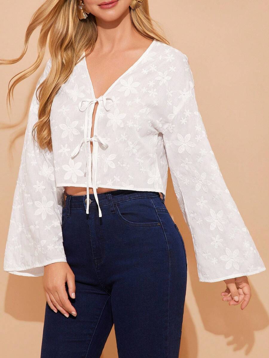 Woman wearing a white blouse with lace-up front and blue jeans on a beige background