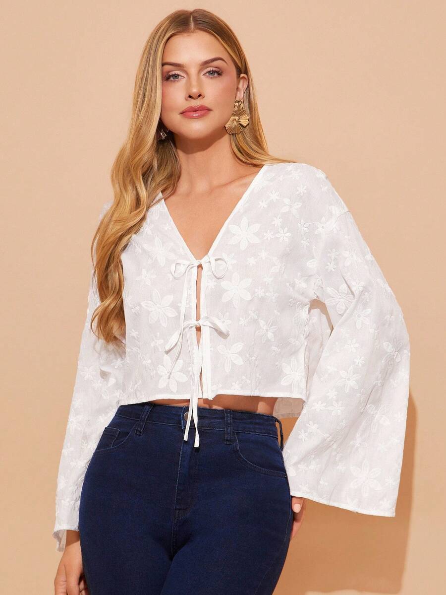 Woman wearing a white blouse with bell sleeves and blue jeans on a beige background