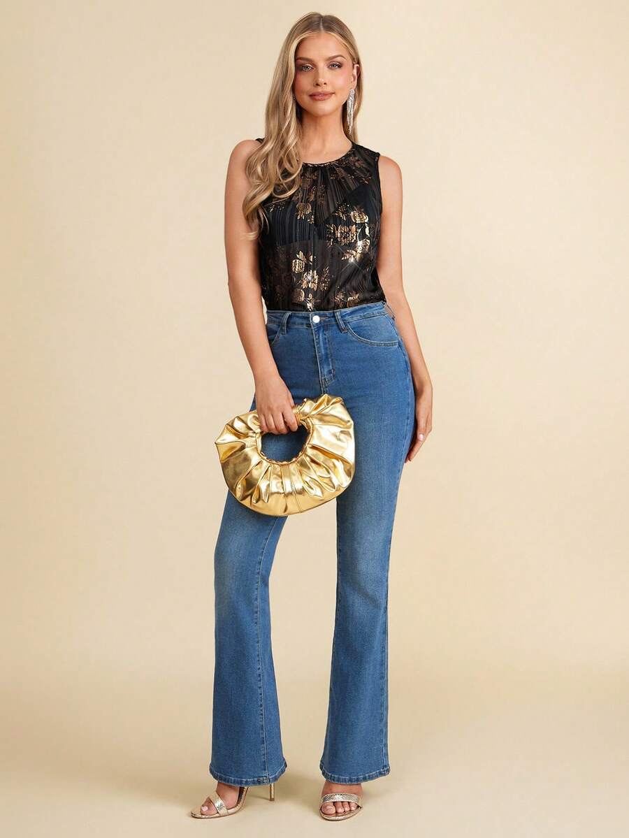 Woman wearing a black floral top and blue jeans, holding a gold clutch against a beige background
