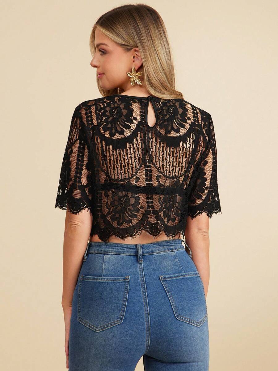 Woman wearing a black lace top and blue jeans on a beige background