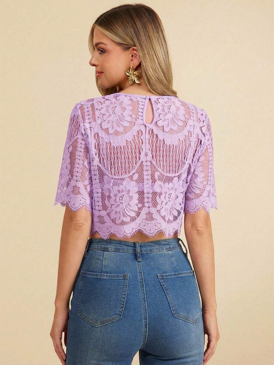 Woman wearing a purple lace top and blue jeans on a beige background
