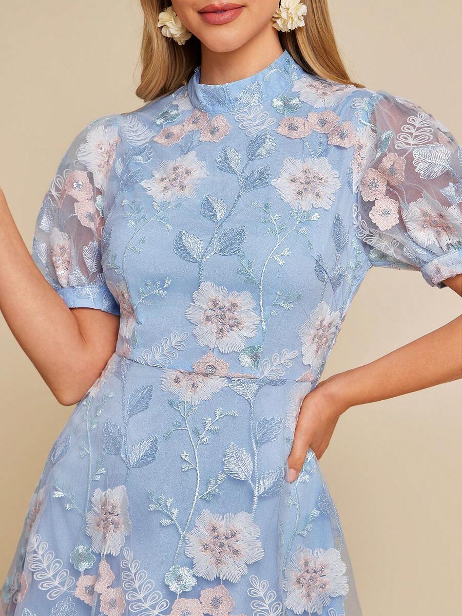 Woman wearing a light blue floral dress with sheer sleeves against a beige background