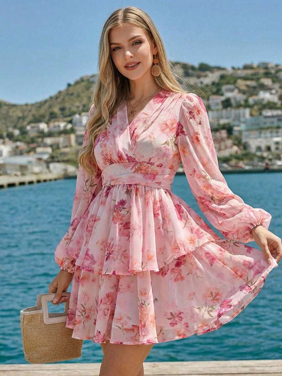 Woman in a pink floral dress standing by a waterfront with a scenic background