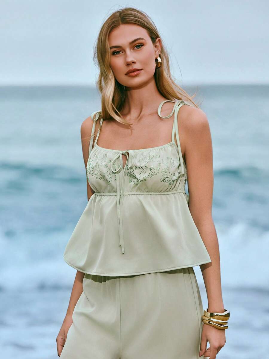 Woman wearing a light green floral top and beige pants standing by the ocean.