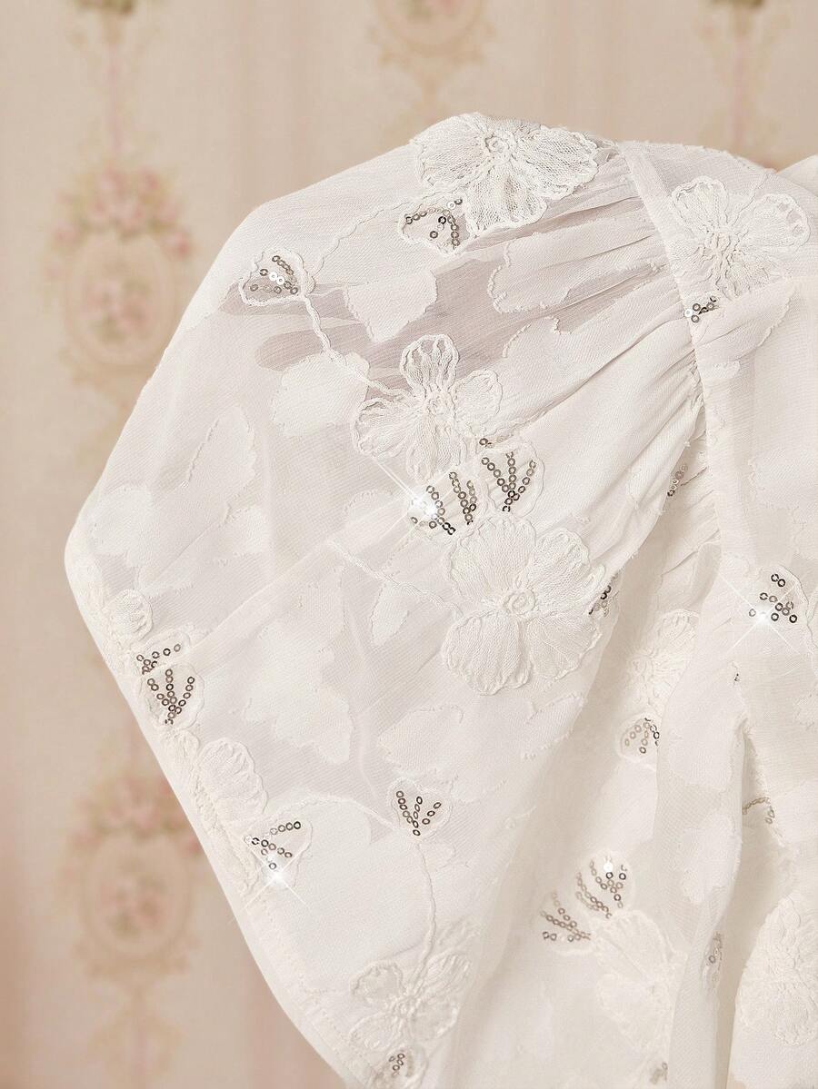 Close-up of a white lace garment with floral embroidery on a soft pink background