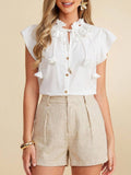 Woman wearing a white blouse with ruffled details and beige shorts on a beige background