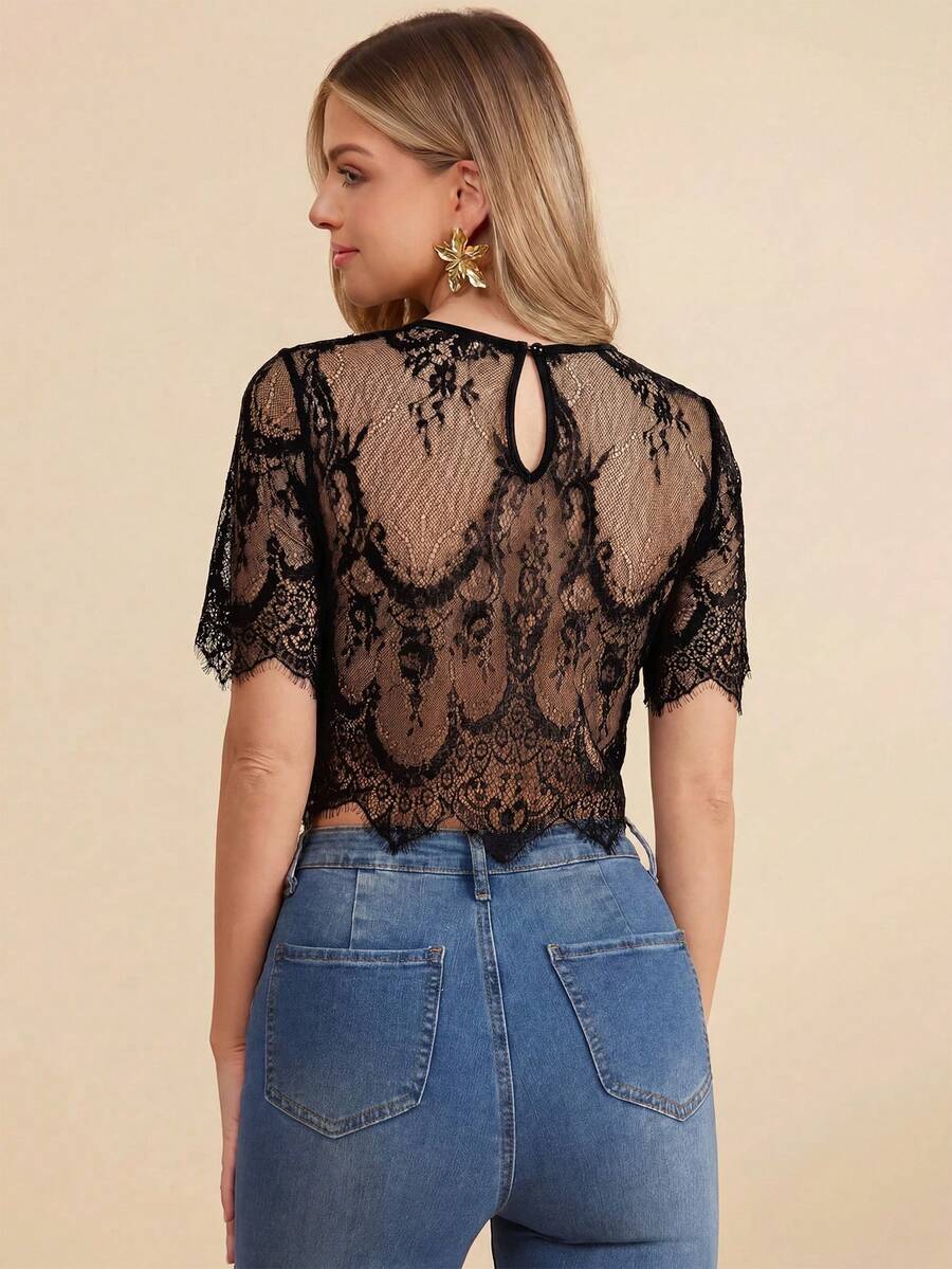 Woman wearing a black lace top and blue jeans on a beige background